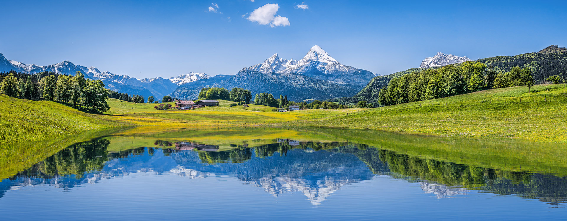 Panoramic view of idyllic summer landscape in the Alps with clear mountain lake and fresh green mountain pastures in the background